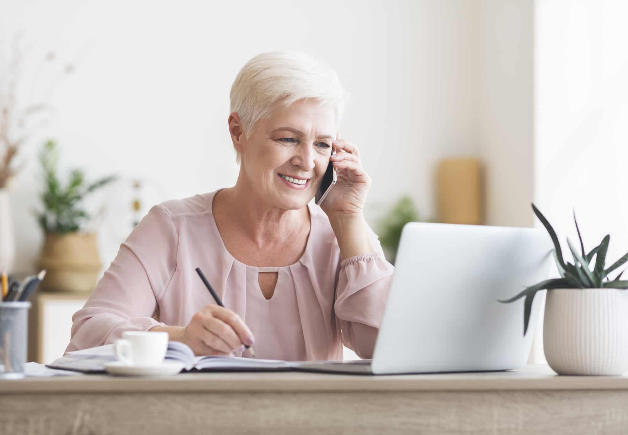 an older woman sitting at a desk and talking on the phone