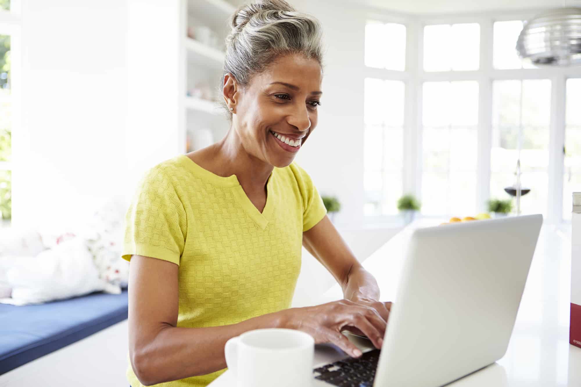 an older woman smiling while working on her laptop